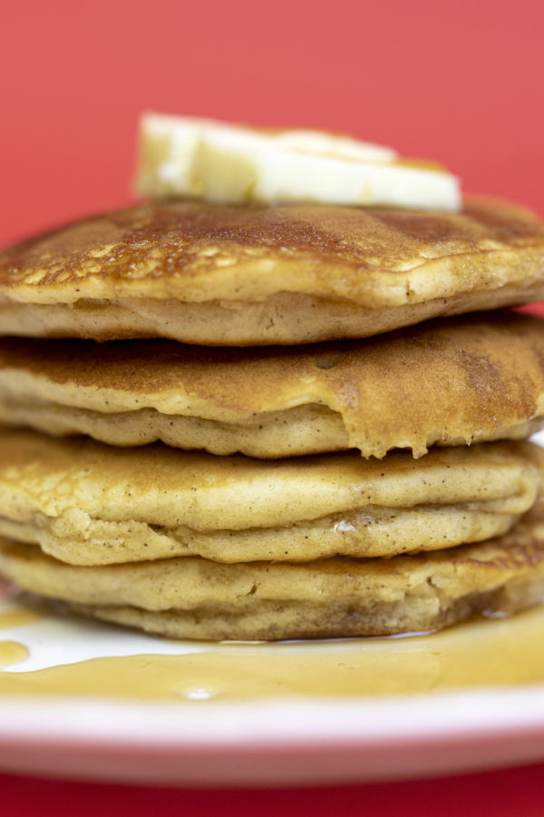 pancakes3 Apple cinnamon pancakes with butter and syrup drizzling over the sides on a white plate with a red backdrop