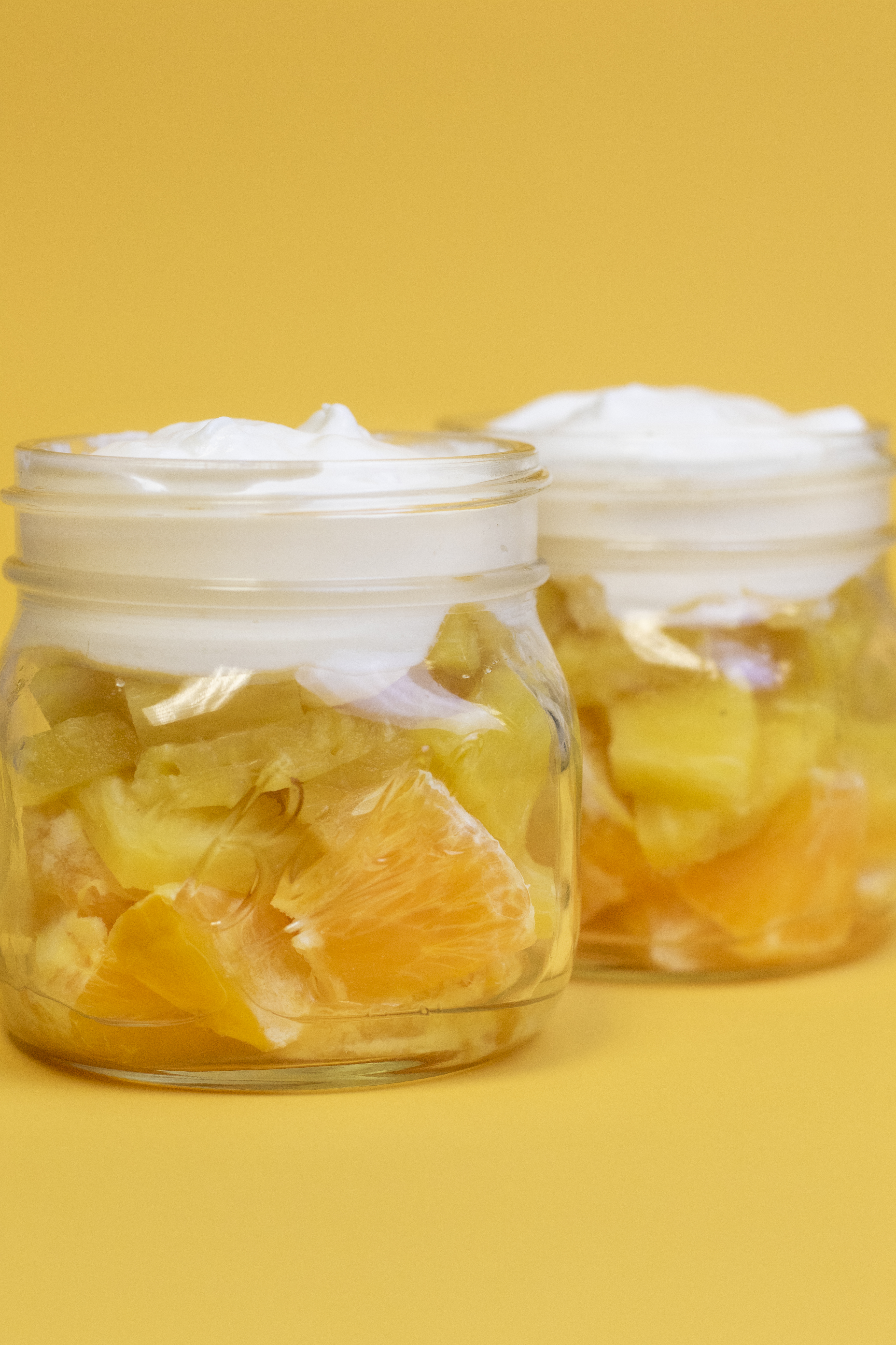 Oranges, pineapple, and whipped topping in a clear mason jar to look like a candy cane on a yellow backdrop.