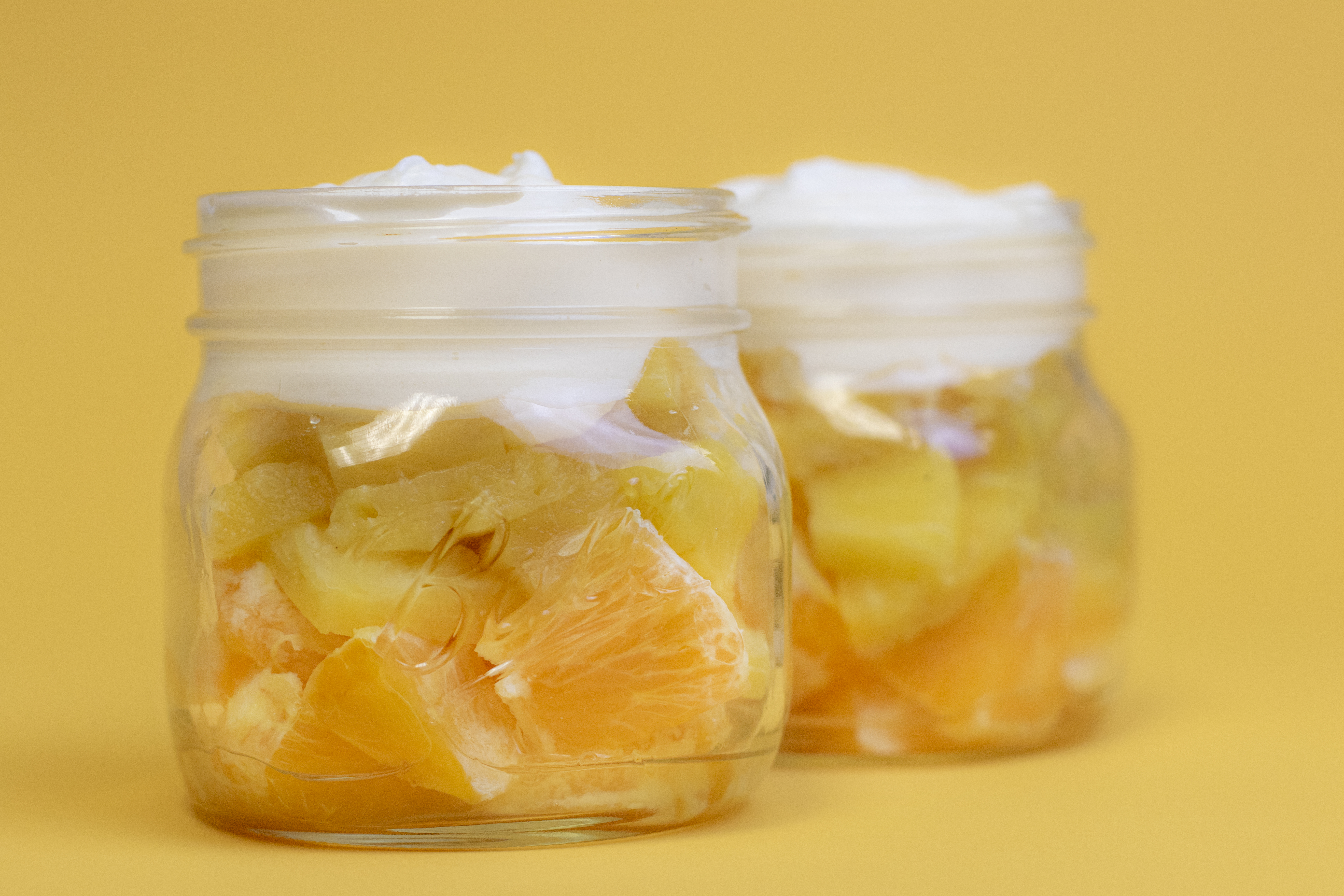 Oranges, pineapple, and whipped topping in a clear mason jar to look like a candy cane on a yellow backdrop.
