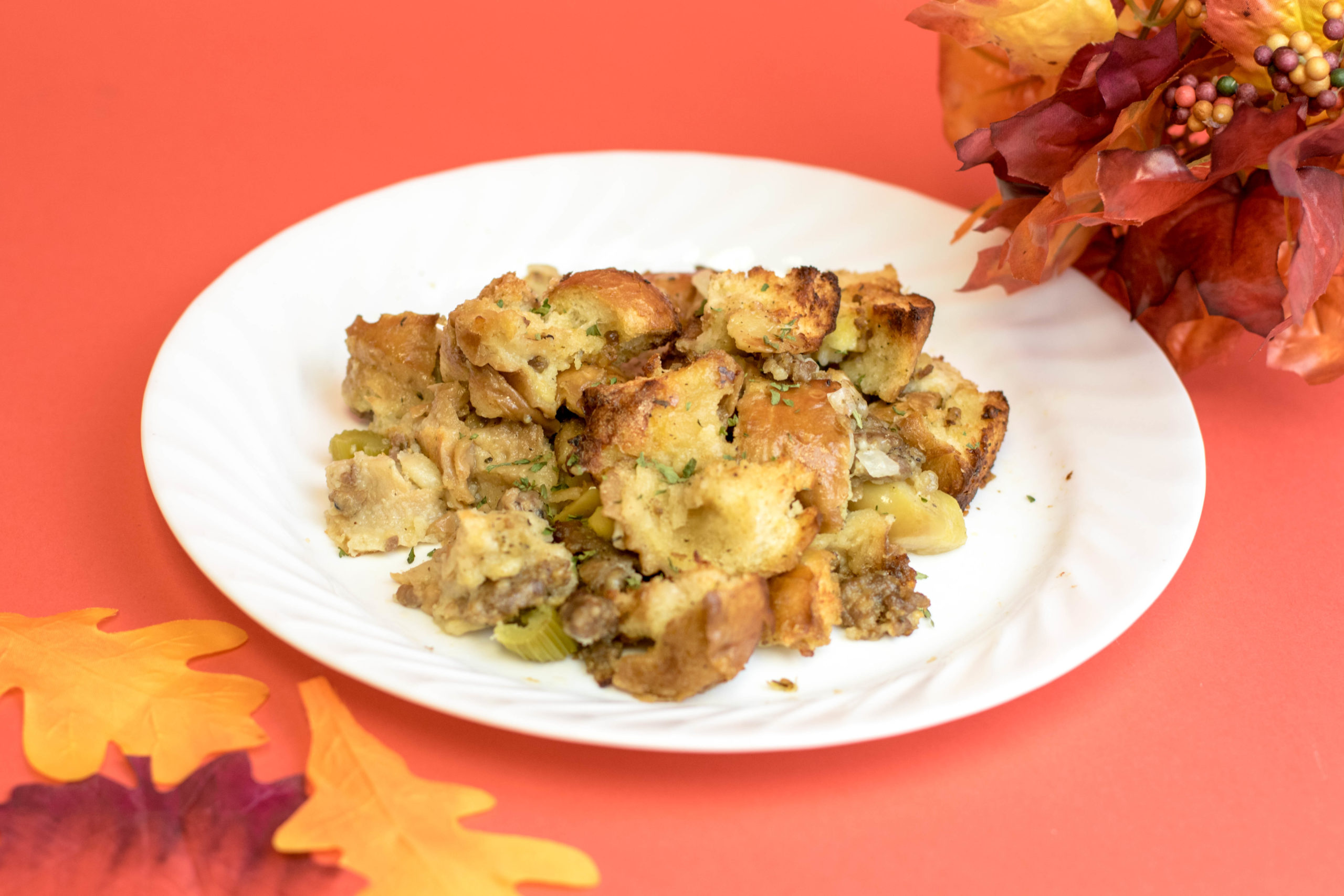 Thanksgiving stuffing on a white plate surrounded by fall leaves sitting on a red background.