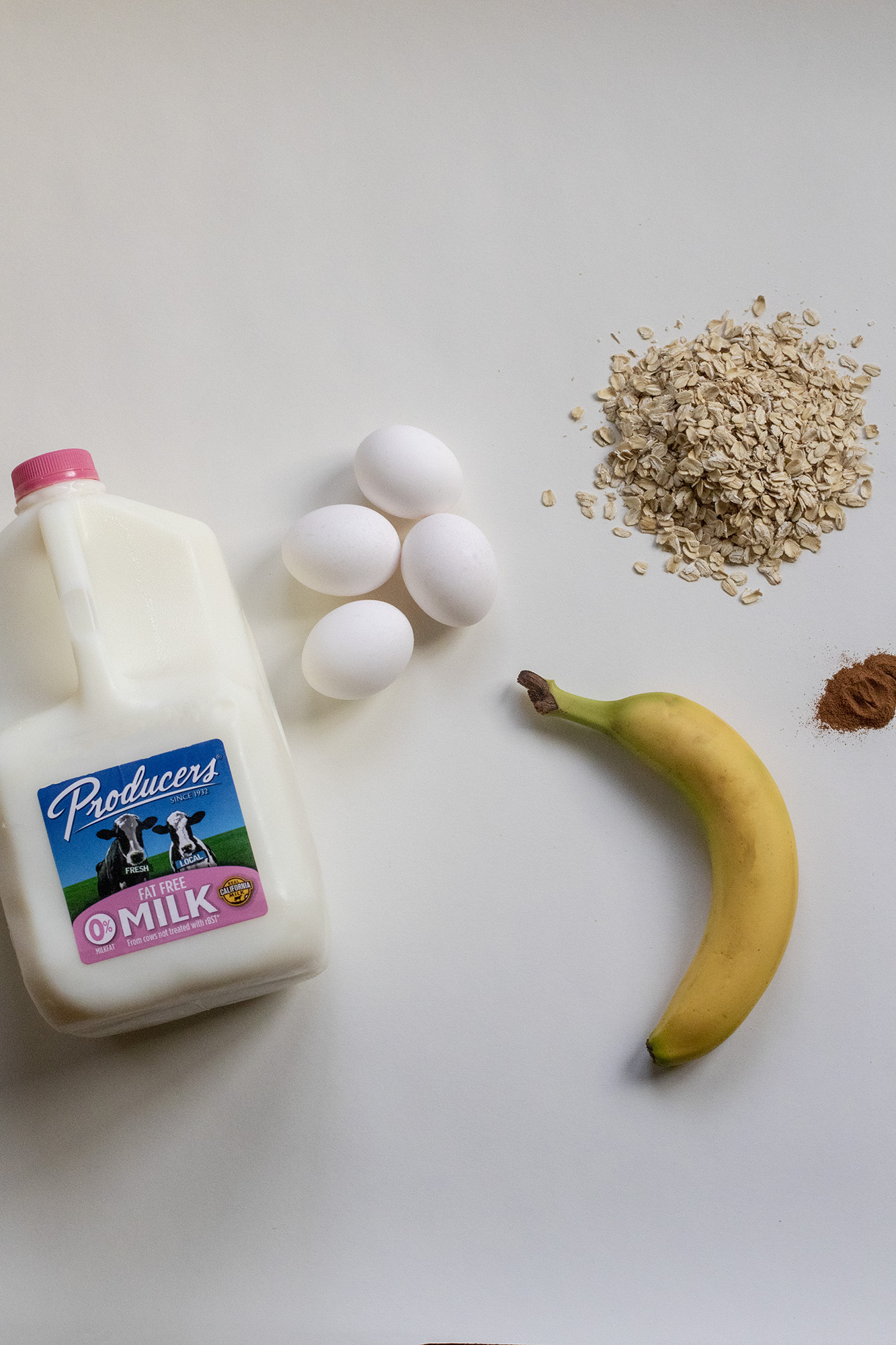 Fat free gallon of Producers milk, 4 eggs, one banana, pile of ads and cinnamon on a white background.
